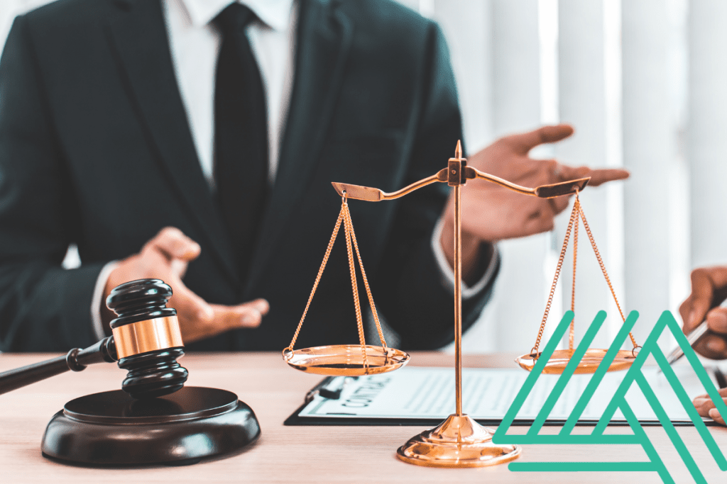 Business person in background, gavel and scale on desk with paperwork