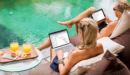 A couple working on their computers whilst holidaying by the pool.